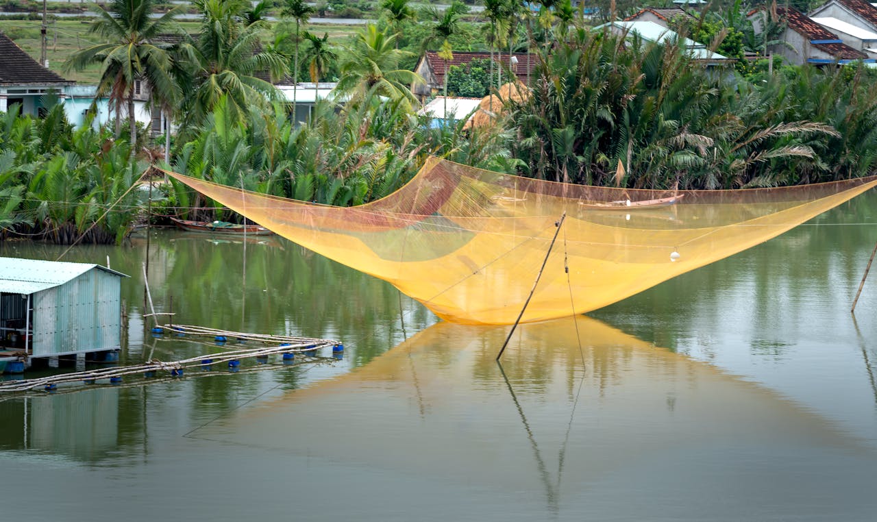A peaceful rural lake scene with a large traditional fishing net and lush greenery.